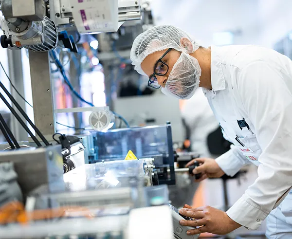 Ein LTS-Mitarbeiter in weißer Arbeitskleidung bedient eine komplexe Fertigungsmaschine in der Produktion.