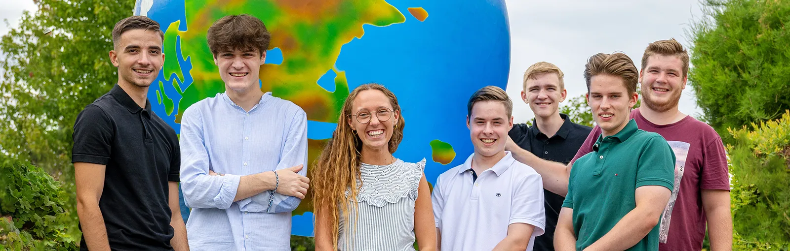 Eine Gruppe von jungen LTS-Mitarbeiter:innen steht lachend vor einem großen Globus im Freien.