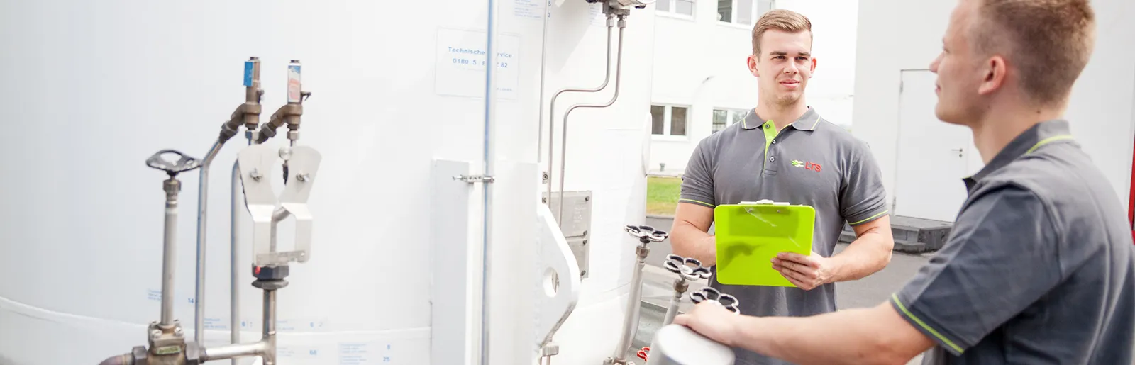 Zwei junge Männer in grauen Poloshirts mit LTS-Logo bedienen eine technische Anlage bei LTS.