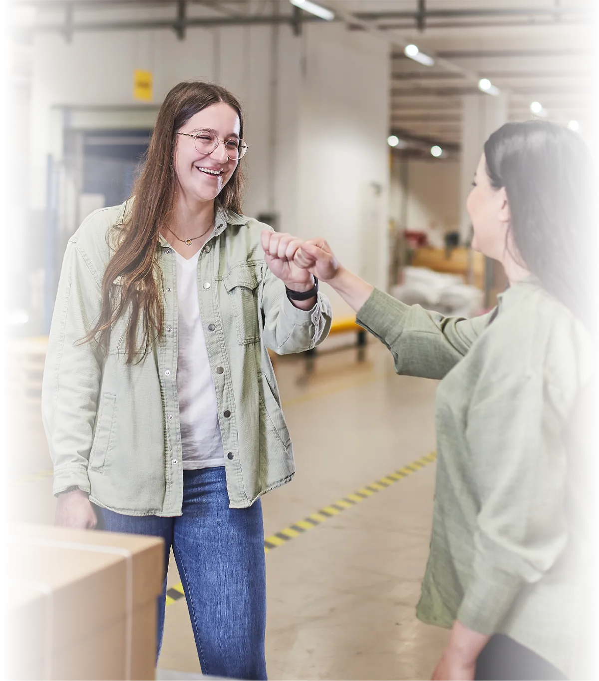 Zwei Frauen begrüßen sich mit einem Faustgruß in moderner Produktionshalle von LTS.